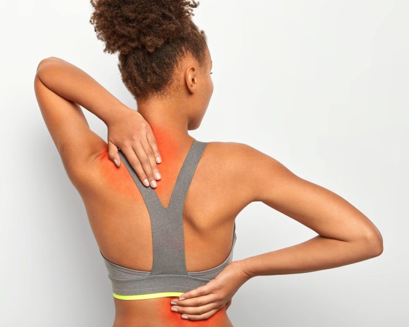 back-view-afro-woman-touches-back-neck-shows-inflammated-zones-poses-against-white-wall-min